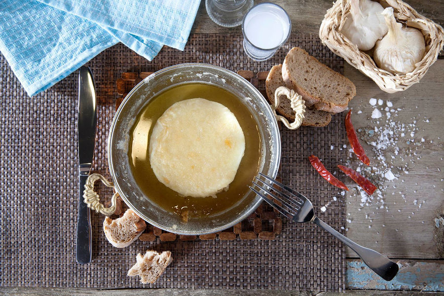view from above of bowl with 'Mystakelli Dairy' white cheese in oil and pieces of dry bread and two garlics